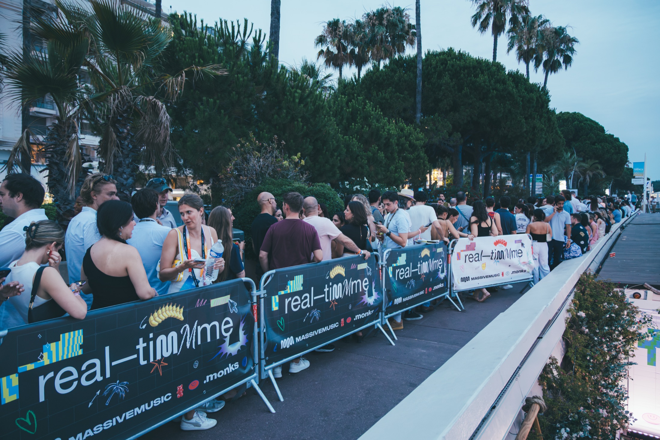 Crowd queuing behind IT'S REAL-TIMMME branded barriers at the party entrance