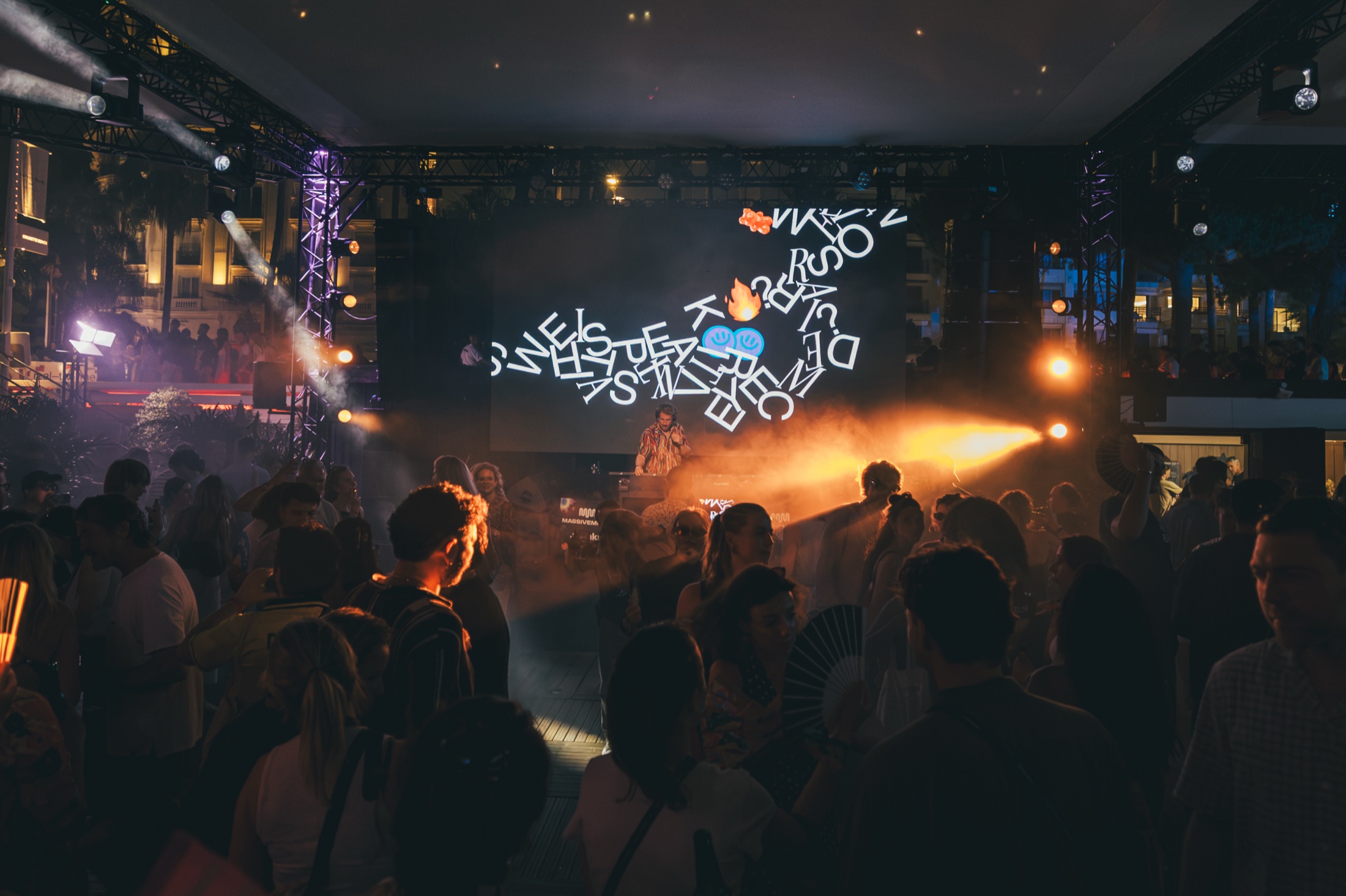 DJ performing under a scrambled animated letters visual as the crowd dances